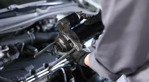 Mechanik w rękawiczkach trzyma rozrusznik. Zastanawiasz się, ile kosztuje wymiana rozrusznika?