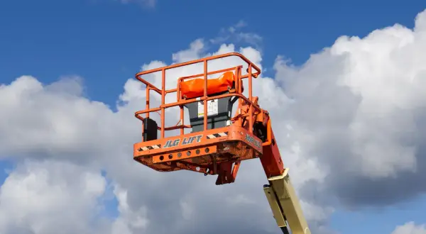 En orange korg från en JLG-lift mot en blå himmel med moln. Säkerhetsanvisningar för mobil arbetsplattform regler är synliga.