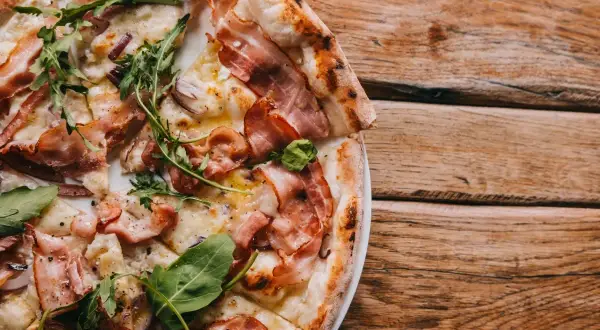 Pyszna pizza carbonara z chrupiącym boczkiem i rukolą, podana na drewnianym blacie.