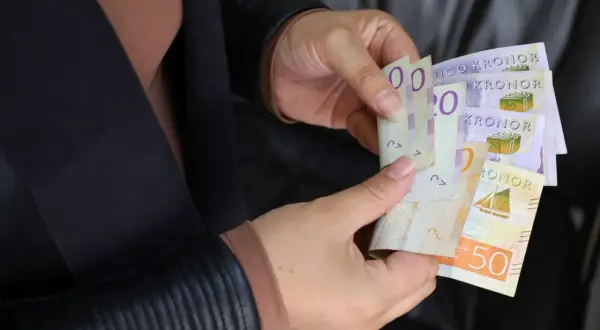 Ręce trzymają banknoty. Czy to sek, jaka to waluta? Widoczne są napisy "KRONOR" i cyfry 20, 50.