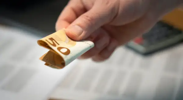 Dłoń trzyma banknot 50 euro. Może to być dodatek dyferencyjny do pensji lub zapłata za usługi.