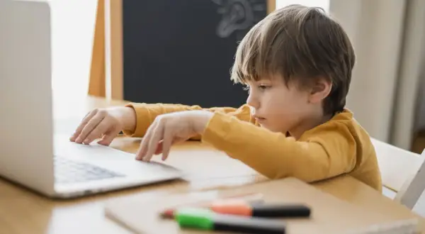 Chłopiec z problemami z koncentracją u dziecka siedzi przy laptopie, zamyślony. Na tablicy rysunek żarówki.