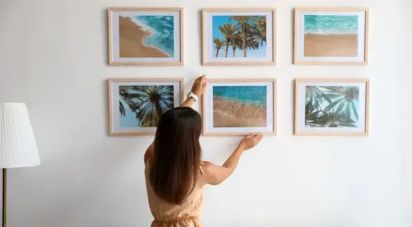 Frau arrangiert Bilder mit Strandmotiven. Tolle bilder anordnen ideen für eine sommerliche Wandgestaltung.