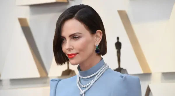 Charlize Theron con un elegante caschetto corto pari, orecchini pendenti e una collana scintillante.