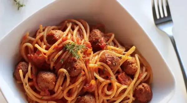 Spaghetti z klopsikami w sosie pomidorowym, udekorowane gałązką tymianku.