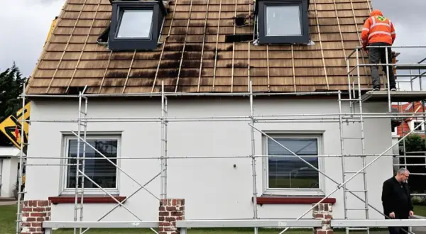Gerüst am Haus, Dach wird saniert. Ein Arbeiter in Warnweste prüft die Arbeiten. Wer kontrolliert Sanierungspflicht?