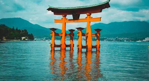 Pomarańczowa brama torii w wodzie, idealne miejsce na Japonia wycieczka. W tle góry i miasto.