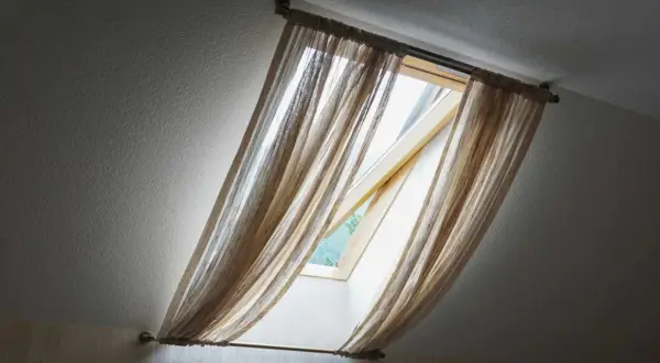 Voilage léger sur un montage store Velux ancien modèle, laissant passer la lumière du jour.