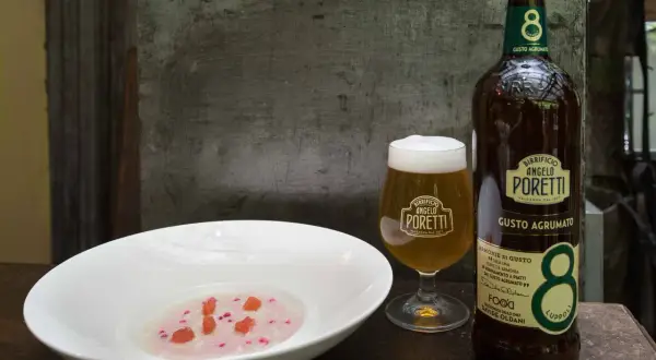 Un bicchiere e una bottiglia di birra Angelo Poretti, una brown ale dal gusto agrumato, accanto a una ciotola con un piatto rosa e pezzetti rossi.