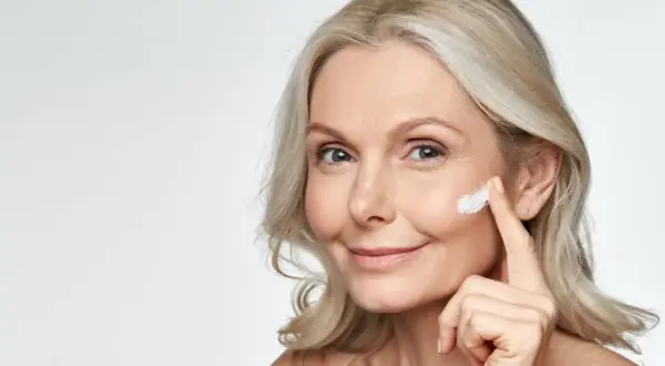 Eine Frau trägt Sonnencreme auf, um Falten vorzubeugen. Jeden Tag Sonnencreme gegen Falten schützt die Haut.