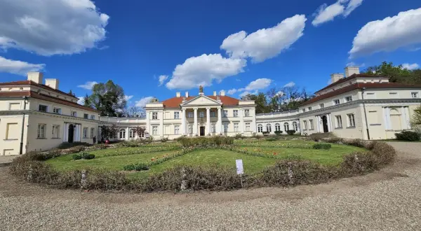 Pałac w stylu klasycystycznym z kolumnami, otoczony ogrodem z kwitnącymi tulipanami. Piękny ląd nad Wartą w słoneczny dzień.