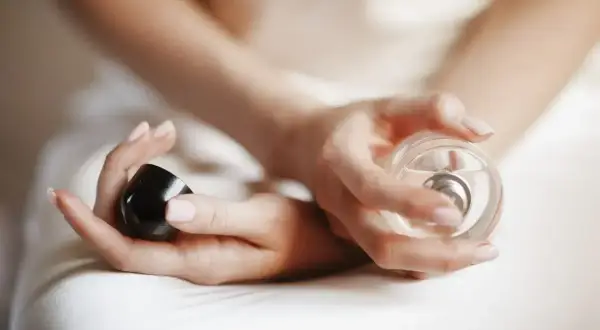 Dłonie kobiety trzymają flakon perfum i czarną nakrętkę. Chcesz wiedzieć, gdzie sprawdzić kod perfum?
