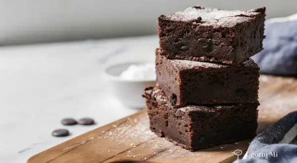 Pyszne, wilgotne brownie z kawałkami czekolady, posypane cukrem pudrem. Idealne na deser według prostego brownie przepisu.