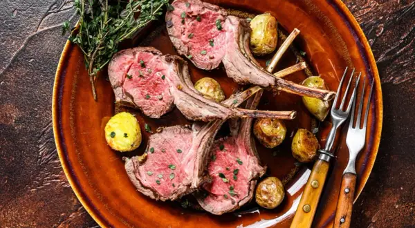 Costolette di agnello in padella, succulente e rosate, servite con patate novelle arrosto e rametti di timo su un piatto di terracotta.