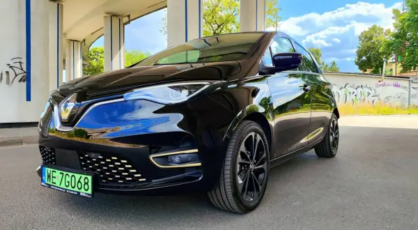 Czarny Renault Zoe błyszczy pod betonowym wiaduktem. Ten elektryczny samochód oferuje imponujący zasięg, idealny na miejskie podróże i dalsze wyprawy.