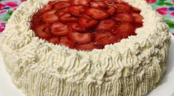 En vacker jordgubbstårta med fluffigt gräddtäcke och ett glansigt jordgubbslager i mitten. Denna ser ut att vara den godaste jordgubbstårtan!