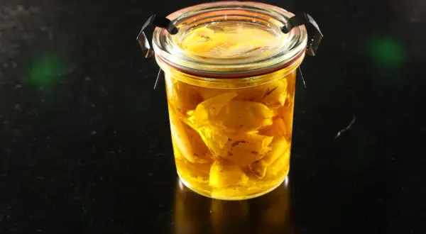 Un bocal en verre rempli d'ail confit dans de l'huile dorée. Les bienfaits de l'ail confit sont nombreux pour la santé.