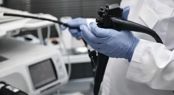 Lekarz w niebieskich rękawiczkach trzyma endoskop. Obok aparatury medycznej, która może wskazywać na zły wynik gastroskopii.