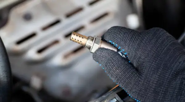 Hand in a glove holds a new auto lambdasonde, ready for installation in a car engine.