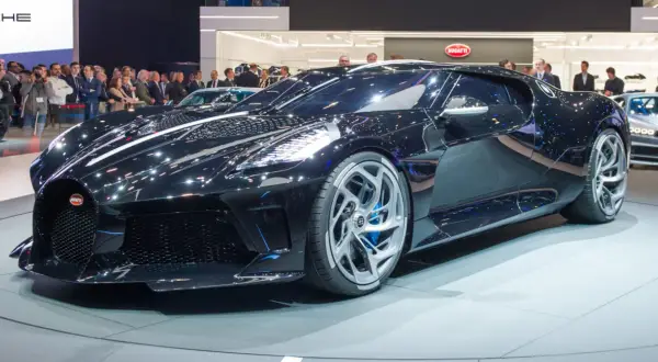 Lśniący, czarny Bugatti La Voiture Noire na wystawie, otoczony tłumem widzów.