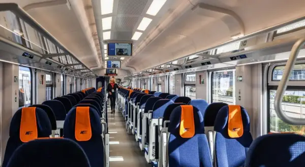 Wnętrze pociągu Intercity. Widok na rzędy niebieskich siedzeń z pomarańczowymi zagłówkami. Czym się różni 1 klasa od 2 w pociągu Intercity?