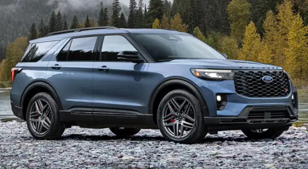Niebieski Ford Explorer ST na kamienistej plaży, z jesiennym lasem w tle.
