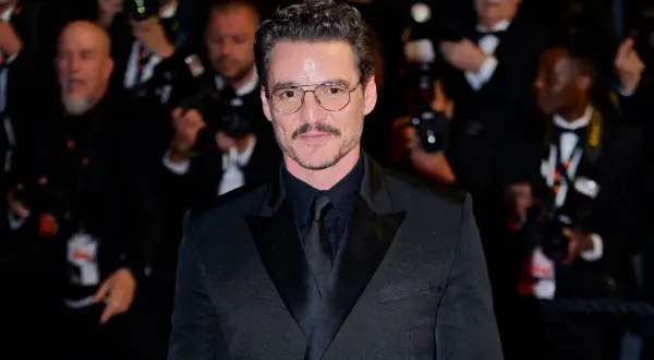 Pedro Pascal sfoggia un impeccabile outfit giacca nera uomo, con camicia e cravatta abbinate, occhiali da vista e baffi.