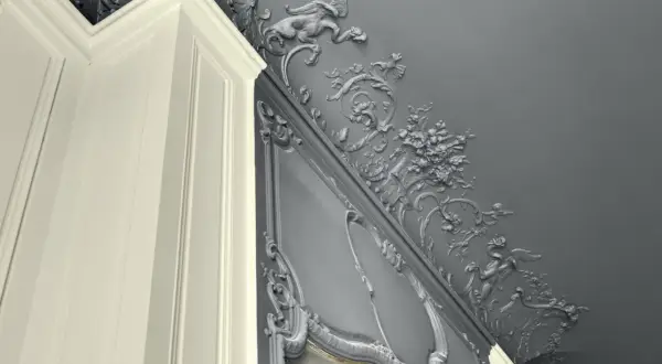 Magnifique peinture velours plafond avis : moulures grises ornées de créatures mythiques et de fleurs, contrastant avec un coin de mur blanc.