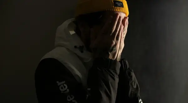 Ein Mann mit gelber Mütze verdeckt sein Gesicht mit den Händen, als ob er mit seinem Gewissen ringt.