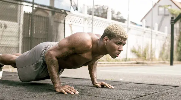 Un homme musclé s'entraîne en extérieur, effectuant des pompes dans un style calisthenics militaire.