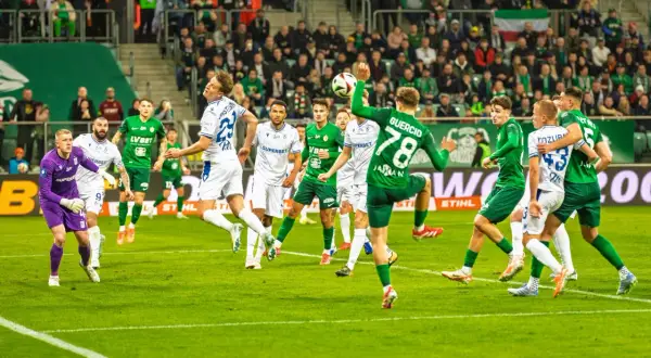 Piłkarze Lecha Poznań w białych strojach i Śląska Wrocław w zielonych grają w piłkę nożną na boisku.