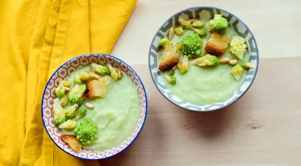 Zwei Schalen cremiger Gemüsesuppe, garniert mit Romanesco, Croutons und Pinienkernen. Ein köstliches Romanesco-Rezept für kalte Tage.