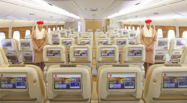 Uśmiechnięta stewardessa w klasie ekonomicznej Emirates. Rzędy wygodnych foteli z ekranami pokładowymi.