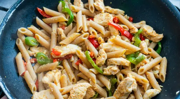 Makaron penne z kurczakiem i papryką w czarnej patelni.