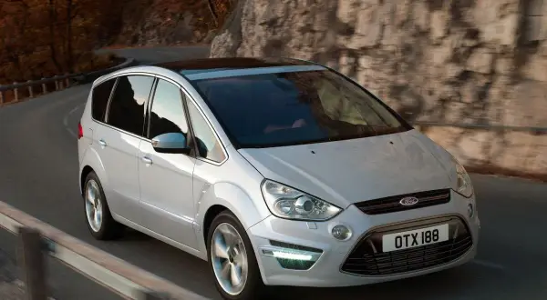 Biały Ford S-Max 2.0 TDCI na krętej drodze wśród jesiennych drzew i skał.