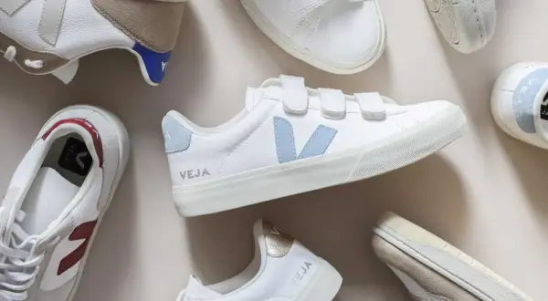 Plusieurs baskets Veja blanches, certaines avec des touches de couleur, sont disposées sur un fond clair. Idéal pour apprendre comment nettoyer des baskets.