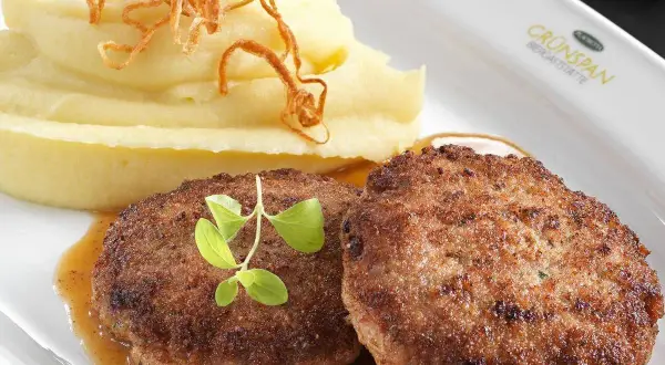 Zwei saftige faschierte Laibchen mit cremigem Kartoffelpüree und knusprigen Röstzwiebeln, garniert mit frischen Kräutern.