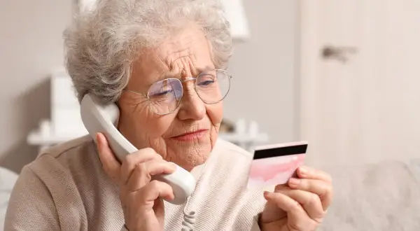 Une femme âgée, sous curatelle renforcée, semble inquiète en tenant une carte bancaire tout en parlant au téléphone.