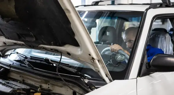 Mechanik sprawdza silnik białego auta. Czy to vaico co to za firma?