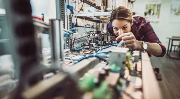 Junge Frau arbeitet konzentriert an einer komplexen Anlage im Bereich IU Elektrotechnik.
