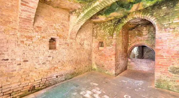 Interno di Santa Maria a Monte: muri in mattoni grezzi, volte muschiose e un arco con una finestra semicircolare.