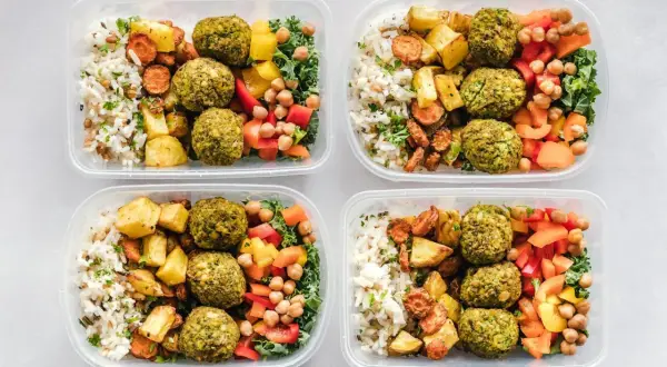 Cztery pojemniki z posiłkami: ryż, pieczone ziemniaki, falafel, warzywa i ciecierzyca.