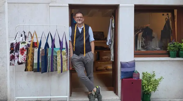 Uomo con metro da sarto nel suo atelier a Venezia. Borse colorate in esposizione.
