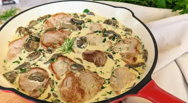 Miękkie polędwiczki wieprzowe w sosie grzybowym, udekorowane koperkiem. Pyszne danie w czerwonej patelni.