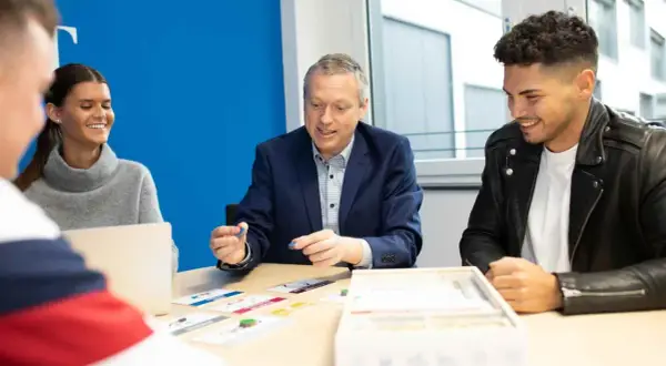 Ein Mann erklärt jungen Leuten beim dualen Studium Marketing Berlin ein Spiel.
