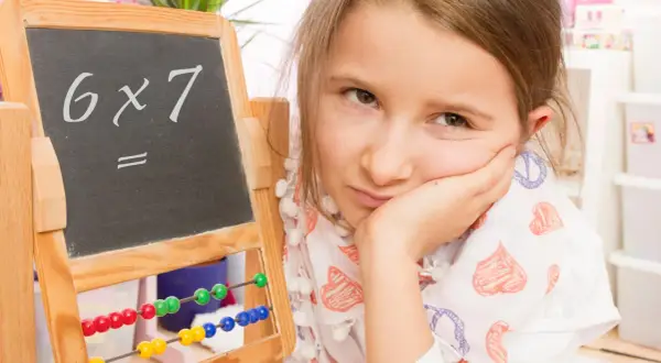 Mädchen mit gelangweiltem Gesichtsausdruck vor einer Tafel mit "6x7=". Vielleicht hilft die Trachtenberg-Methode beim Rechnen.