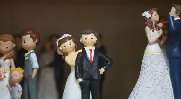 Figurines de couples mariés, certaines avec des enfants, sur un fond flou.