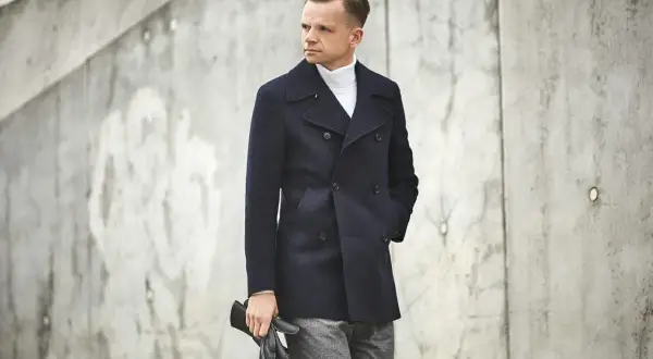Elegancki mężczyzna w granatowej bosmance i białym golfie, trzymający czarne rękawiczki.