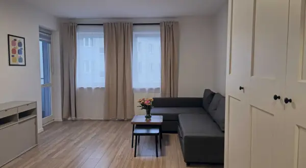 Nowoczesny salon z szarą kanapą, stolikiem kawowym z kwiatami i dużymi oknami.