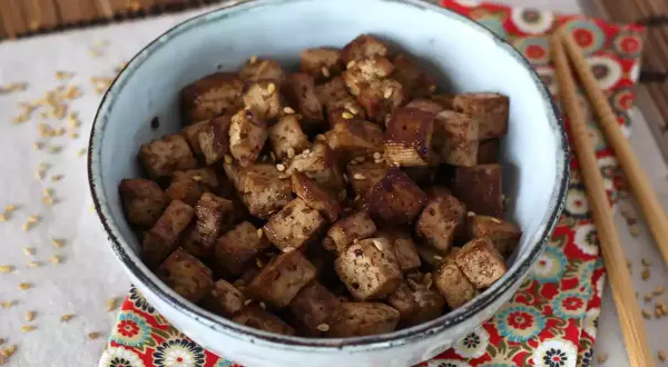 En skål med krispiga, tärnade tofu bitar, glaserade i en smakrik, glutenfri marinad och toppade med sesamfrön.